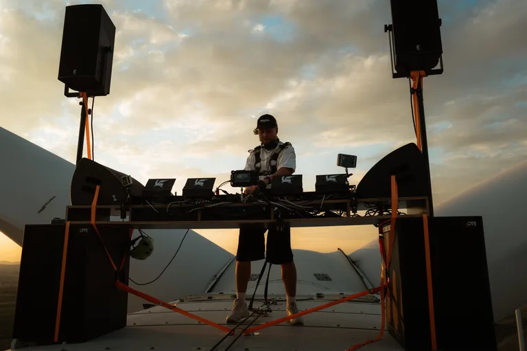 DJ-Set auf dem Gondeldach, links und rechts die Rotorblätter, Lautsprecher auf Stativen