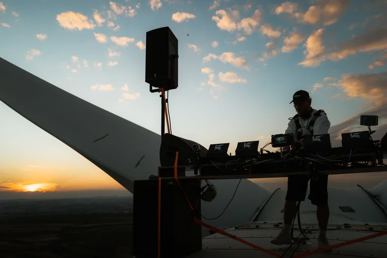 Enei am DJ-Pult auf dem Dach einer Windradgondel bei Sonnenuntergang