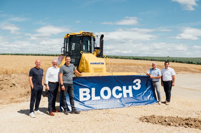 Fünf Personen vor einer gelben Baumaschine und einem BLOCH3-Banner auf einem Feld in Maustrenk