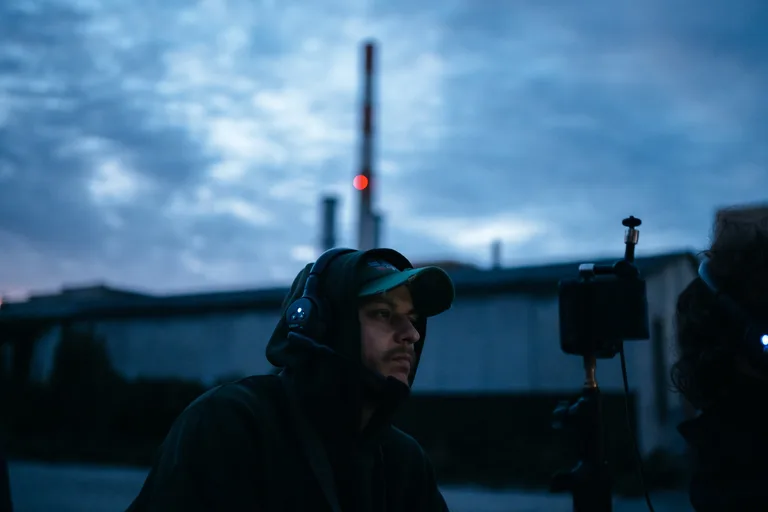 Dreh für Guilty in der Dämmerung: Crew-Mitglied mit Headset vor einem Industrieschlot mit rotem Warnlicht